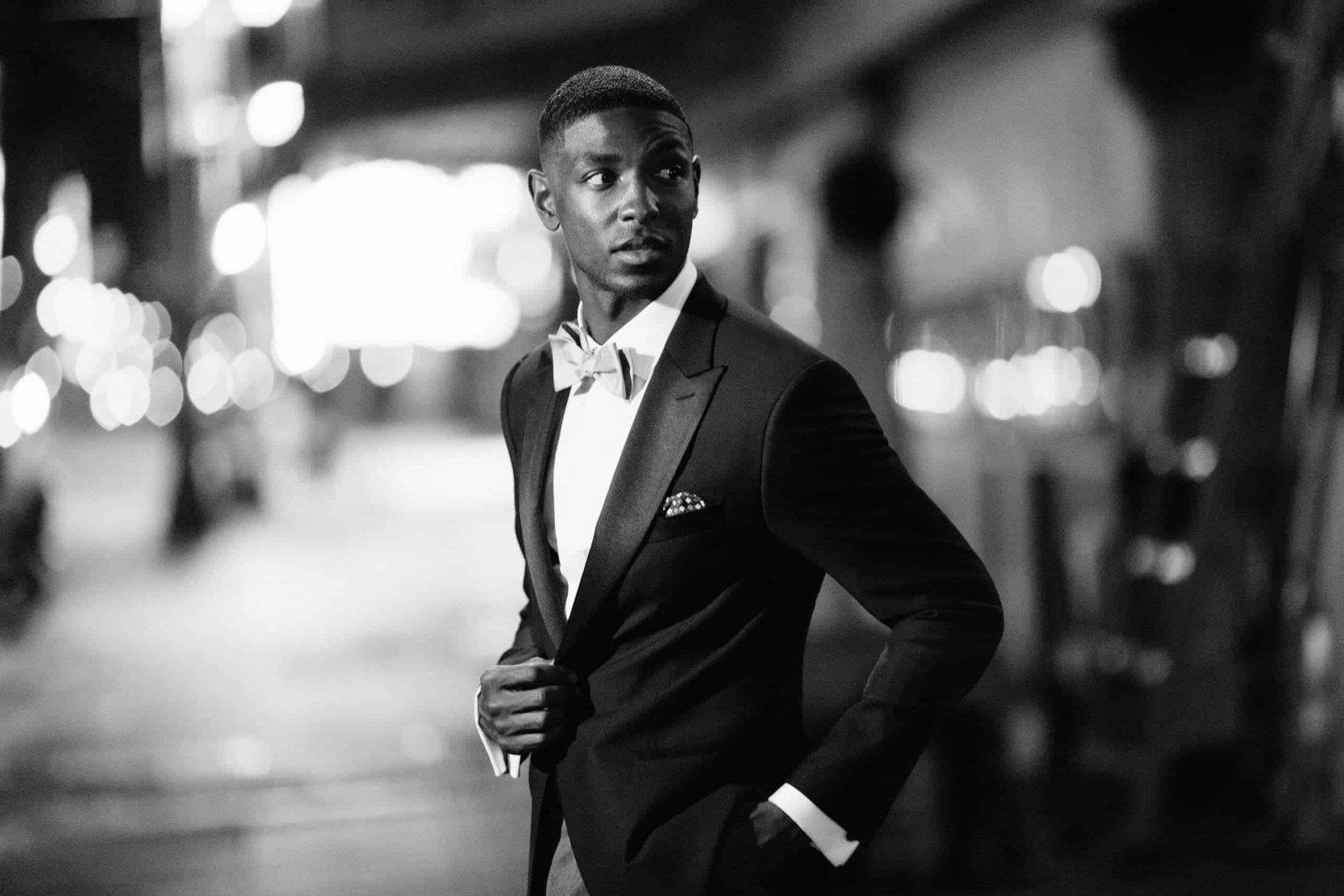 A black and white photo of a man in a black tuxedo standing in the street. Kansas City suit rental