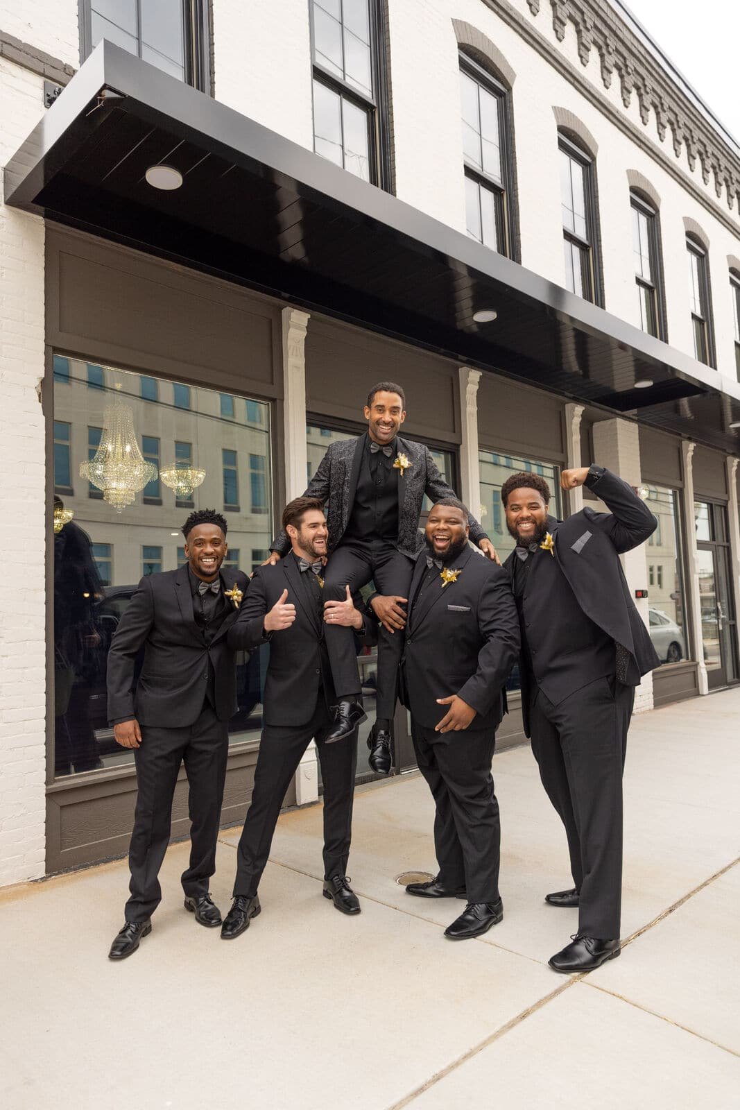 groomsmen holding up a groom on their shoulders wearing black suits. Suit rental Kansas City