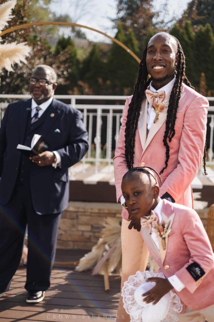 a father and son standing at the alter both wearing pink and champagne tuxedos