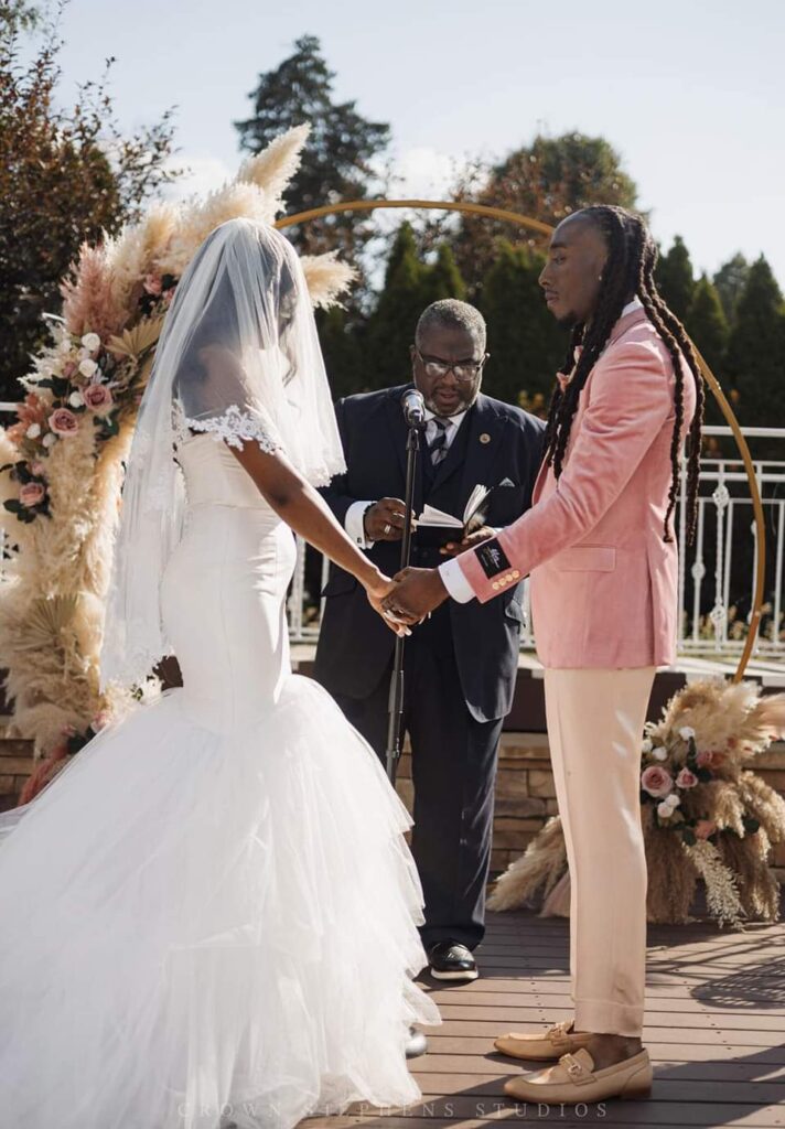 A bride and groom in a pink and champagne tuxedo standing at the alter holding hands.