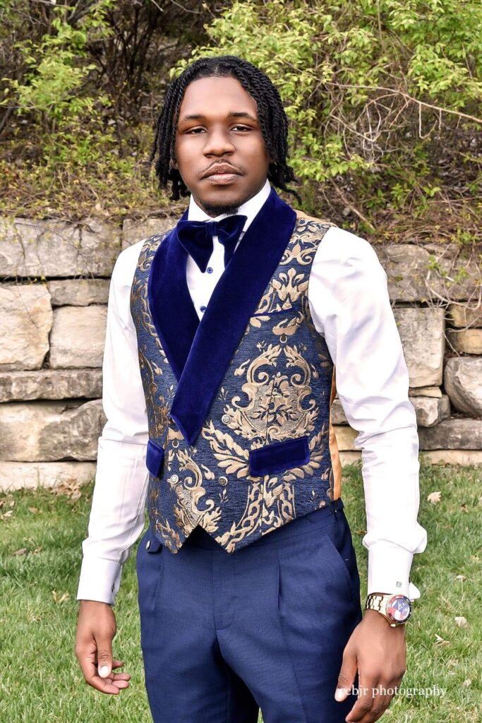 A teen in a blue and gold jacquard tuxedo standing outside