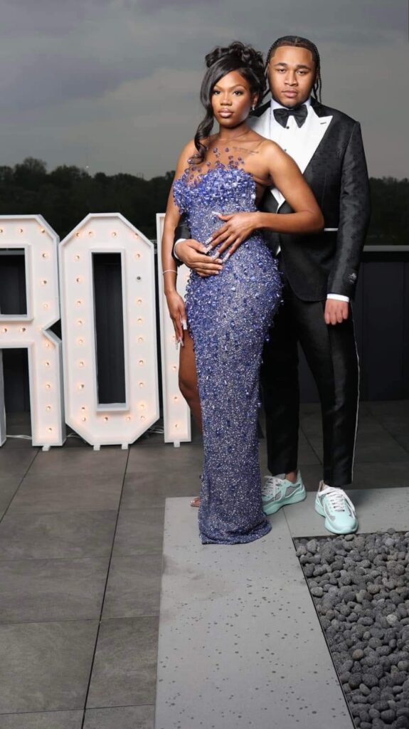 A boy and girl standing wearing a black and white tuxedo and Blue gown