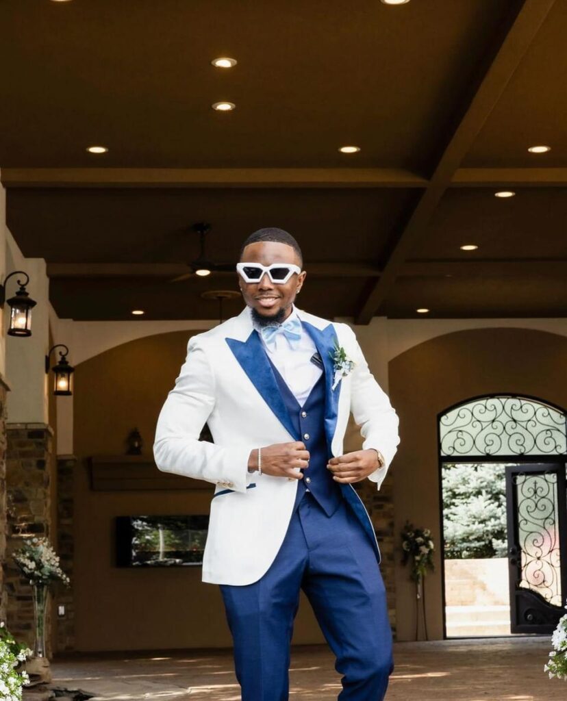 A man in a cream and blue tuxedo standing outside, opening his jacket