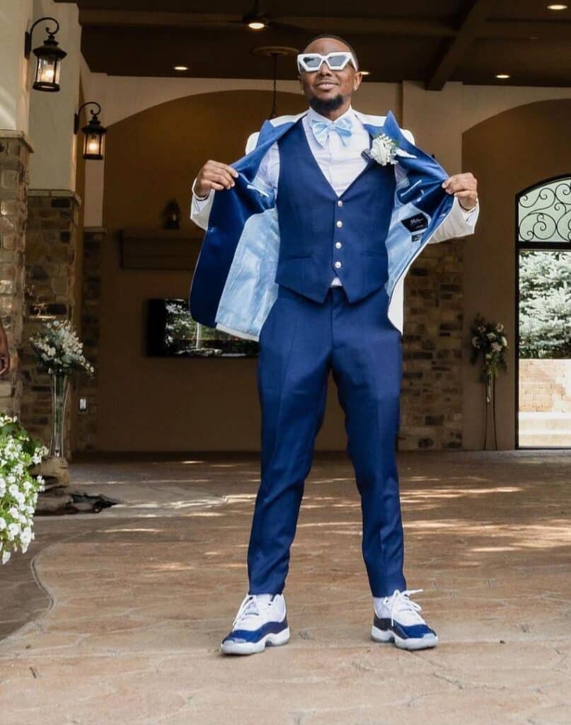 A man in a cream and blue tuxedo standing outside, opening his jacket