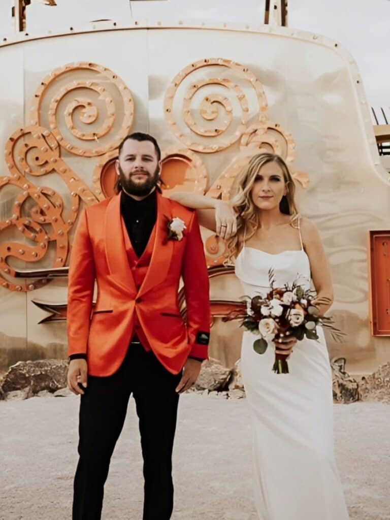 A bride and groom standing in front of a backdrop. Custom Suits Kansas City