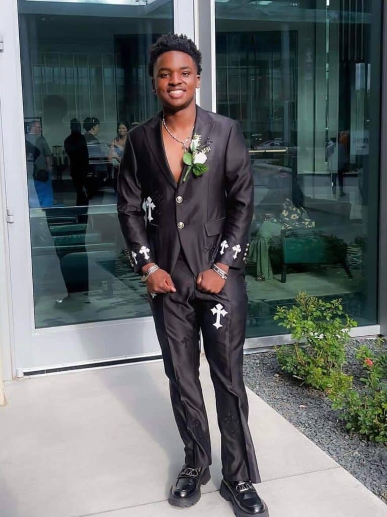 A boy standing outside wearing a black custom suit with black and white crosses on it.